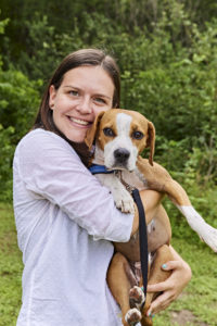 mujer con perro de pie delante de un fondo verde