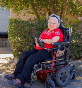 Renee López, ex miembro de la Junta Directiva, sentada en una silla de ruedas hecha a medida y sonriendo.